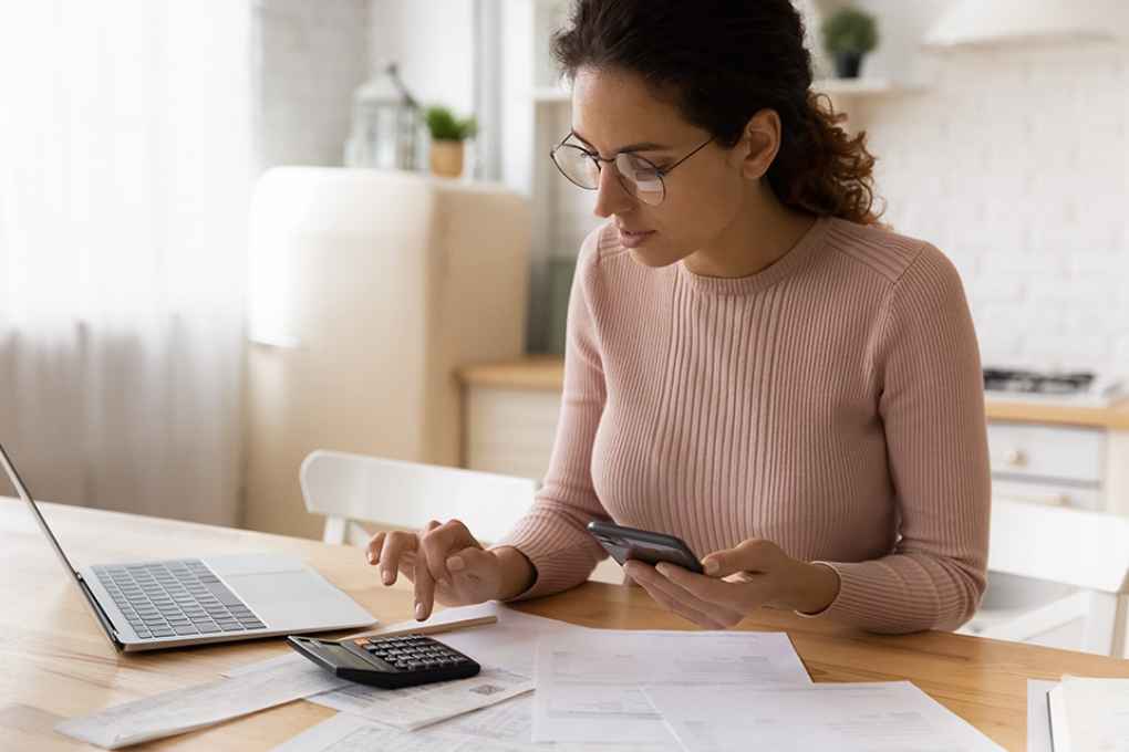 © fizkes - stock.adobe.com Foto: Frau mit Smartphone, Taschenrechner und Laptop